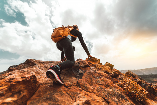 young woman with backpack climbs mountain top