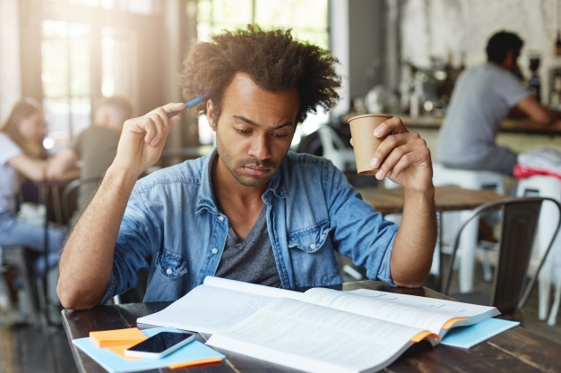 Black man reading books with pen on his full hair