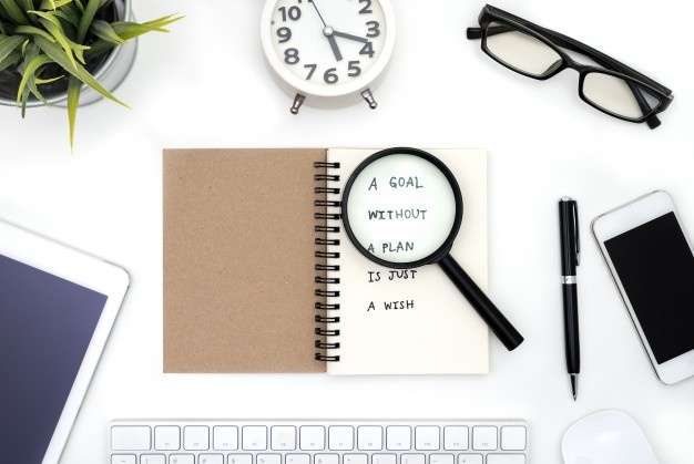 Magnifying glass on book, with glasses, pen and phones and tablet beside it