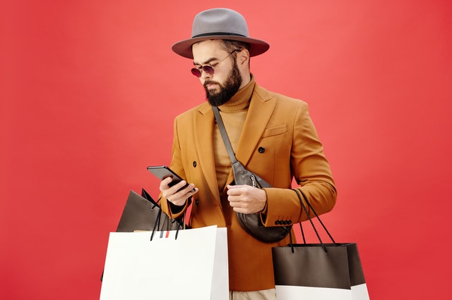 man in a brown blazer carrying shopping bags while using his cell phone